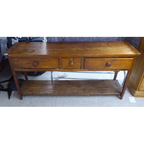 147 - An early 20thC pine dresser with three inline drawers, raised on tapered legs, united by a platform ... 