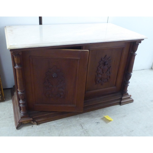 162 - A Continental Edwardian inspired pine side cabinet with a sit-on marble top, over a pair of carved, ... 