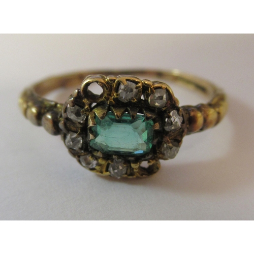 193 - A yellow metal cluster ring, set with a central emerald, surrounded by diamonds (two missing)