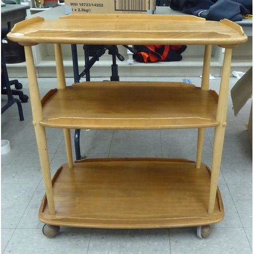 369 - An Ercol blonde beech and elm framed, three tier serving trolley, raised on turned supports and cast... 