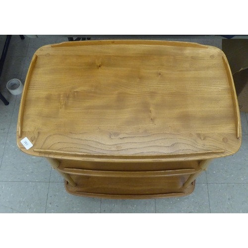 369 - An Ercol blonde beech and elm framed, three tier serving trolley, raised on turned supports and cast... 