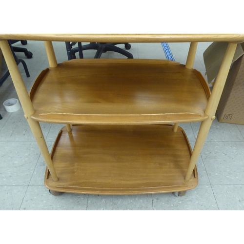 369 - An Ercol blonde beech and elm framed, three tier serving trolley, raised on turned supports and cast... 