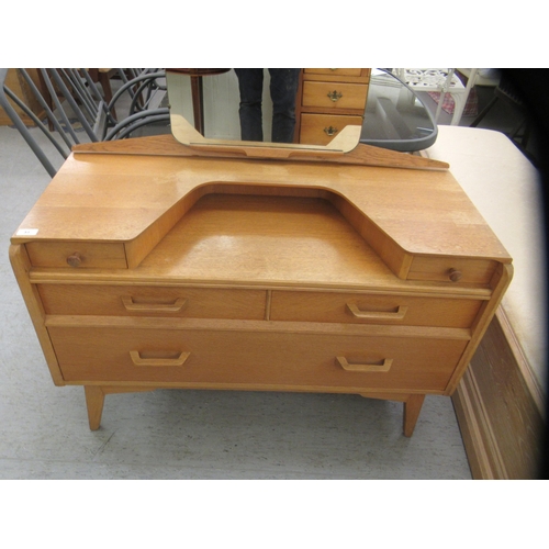 51 - A G-Plan light oak dressing table, surmounted by an unframed mirror, over an arrangement of short an... 