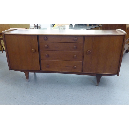 89 - A 1970s teak bow front sideboard with a central bank of four drawers, flanked by two doors, raised o... 