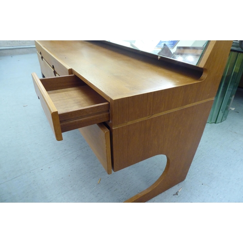 91 - A 1970s teak dressing table, surmounted by an angled mirror, over six drawers, raised on panelled en... 