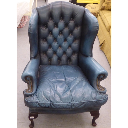 144 - A modern Chesterfield style wingback library chair, part button and stud upholstered in blue hide, r... 