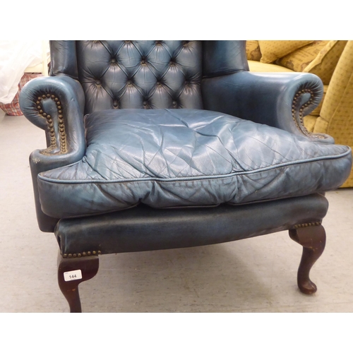 144 - A modern Chesterfield style wingback library chair, part button and stud upholstered in blue hide, r... 