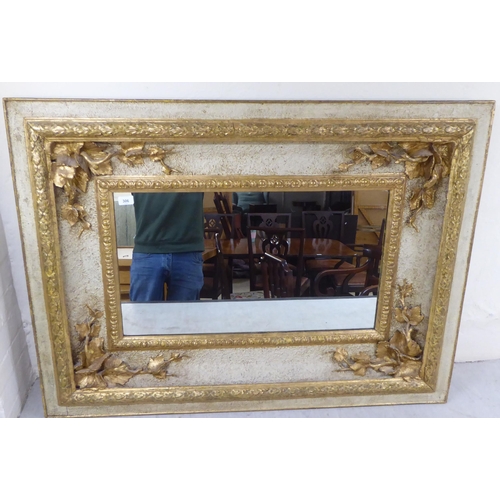 306 - An early 20thC mirror, set in an extravagantly moulded parcel gilt and painted, textured wooden fram... 