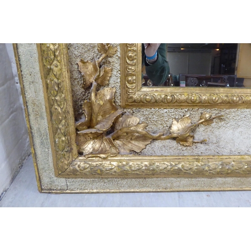 306 - An early 20thC mirror, set in an extravagantly moulded parcel gilt and painted, textured wooden fram... 