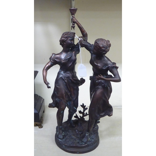 247 - An early 20thC bronze group, two women, one holding aloft a torch, on a circular plinth  bears ... 