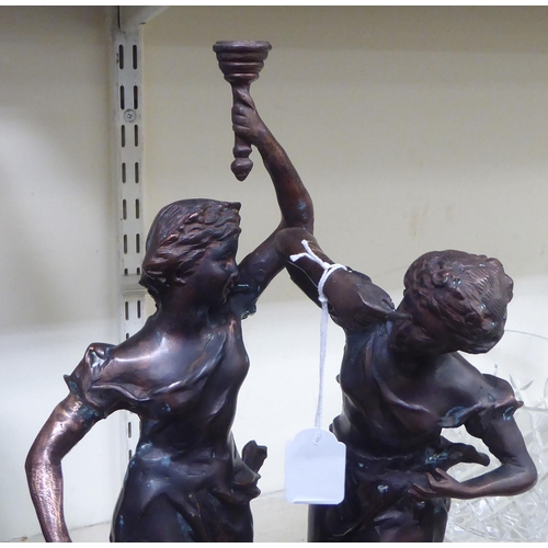 247 - An early 20thC bronze group, two women, one holding aloft a torch, on a circular plinth  bears ... 