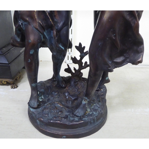 247 - An early 20thC bronze group, two women, one holding aloft a torch, on a circular plinth  bears ... 