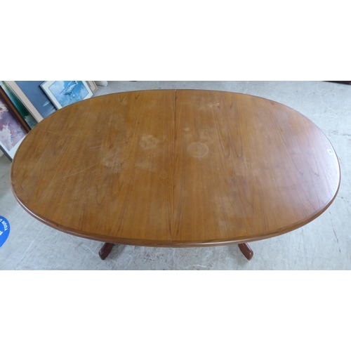 308 - A modern teak extending dining table, the oval top incorporating an integrated additional leaf, rais... 