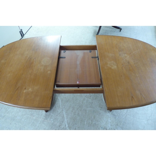 308 - A modern teak extending dining table, the oval top incorporating an integrated additional leaf, rais... 