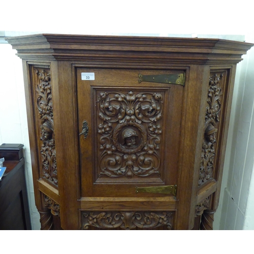 33 - A late 19th/early 20thC Continental light oak credence style cupboard with heavily carved ornament, ... 