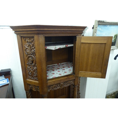 33 - A late 19th/early 20thC Continental light oak credence style cupboard with heavily carved ornament, ... 