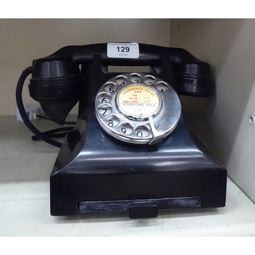 129 - A mid 20thC black Bakelite telephone on a cradle with a rotating dial, over a base drawer