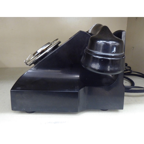 129 - A mid 20thC black Bakelite telephone on a cradle with a rotating dial, over a base drawer