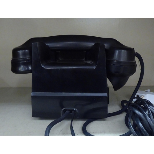 129 - A mid 20thC black Bakelite telephone on a cradle with a rotating dial, over a base drawer