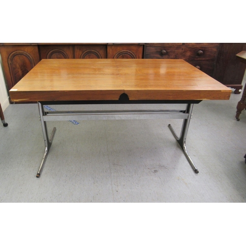 275 - In the manner of Heals, a 1970s rosewood veneered draw action dining table, raised on a cast metal a... 