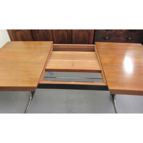 275 - In the manner of Heals, a 1970s rosewood veneered draw action dining table, raised on a cast metal a... 