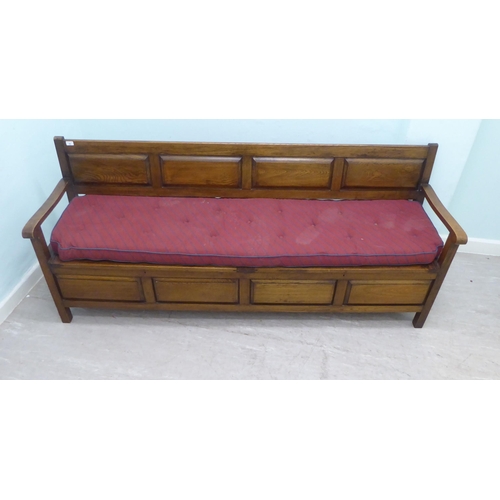 36 - An early/mid 20thC oak bench with a panelled back and open arms, over two hinged box seats, raised o... 