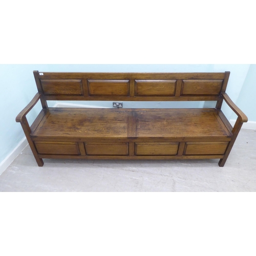 36 - An early/mid 20thC oak bench with a panelled back and open arms, over two hinged box seats, raised o... 