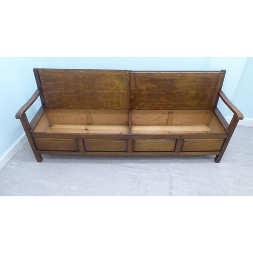 36 - An early/mid 20thC oak bench with a panelled back and open arms, over two hinged box seats, raised o... 