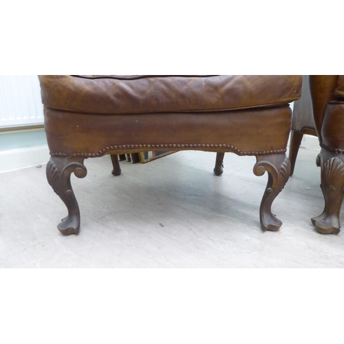 46 - A pair of 1920s/30s simulated brown hide upholstered wingback library chairs, raised on stained beec... 