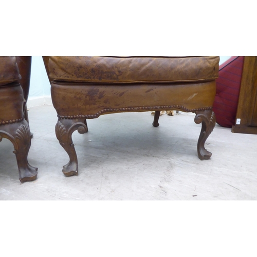 46 - A pair of 1920s/30s simulated brown hide upholstered wingback library chairs, raised on stained beec... 