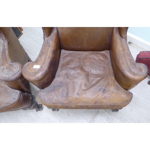 46 - A pair of 1920s/30s simulated brown hide upholstered wingback library chairs, raised on stained beec... 