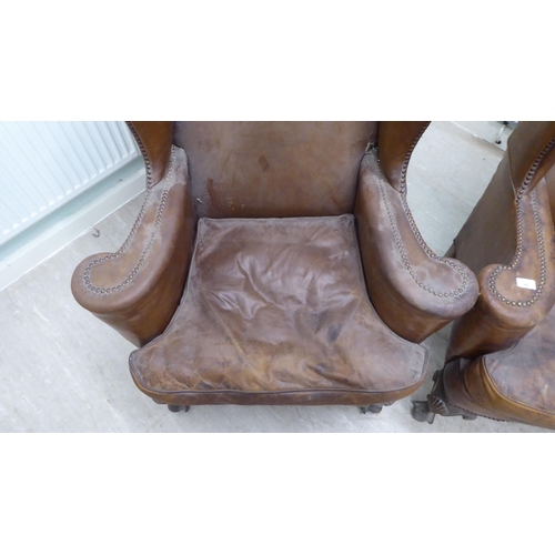 46 - A pair of 1920s/30s simulated brown hide upholstered wingback library chairs, raised on stained beec... 