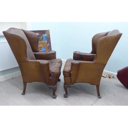 46 - A pair of 1920s/30s simulated brown hide upholstered wingback library chairs, raised on stained beec... 