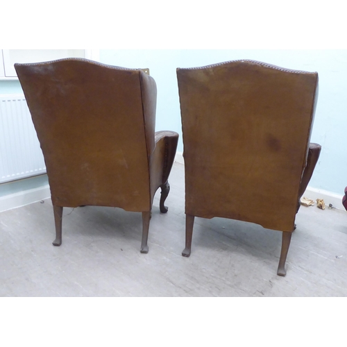 46 - A pair of 1920s/30s simulated brown hide upholstered wingback library chairs, raised on stained beec... 