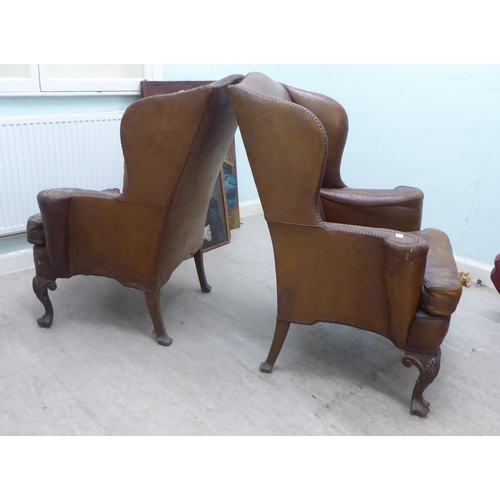 46 - A pair of 1920s/30s simulated brown hide upholstered wingback library chairs, raised on stained beec... 