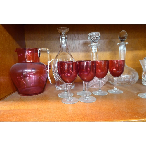 12 - Glassware: to include a clear and cranberry coloured cordial jug and six decanters