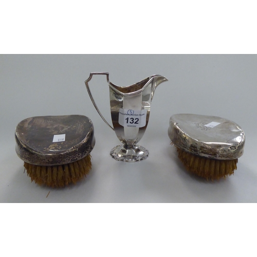 132 - A pair of silver backed hairbrushes; and a silver helmet shaped, octagonal, pedestal cream jug ... 