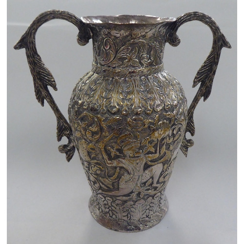 136 - An Indian white metal on copper twin handled vase, profusely decorated with figures, animals and fol... 