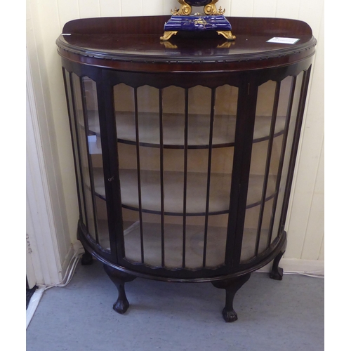 33 - A 1930s mahogany bow front display cabinet, the central door enclosing two shelves, raised on talon ... 