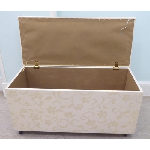 46 - A modern cream coloured fabric upholstered ottoman with straight sides and a cushioned, hinged seat,... 