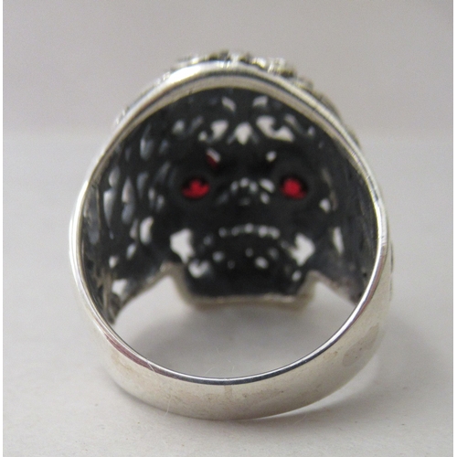 34 - A silver coloured metal ring, featuring a skull with red glass eyes