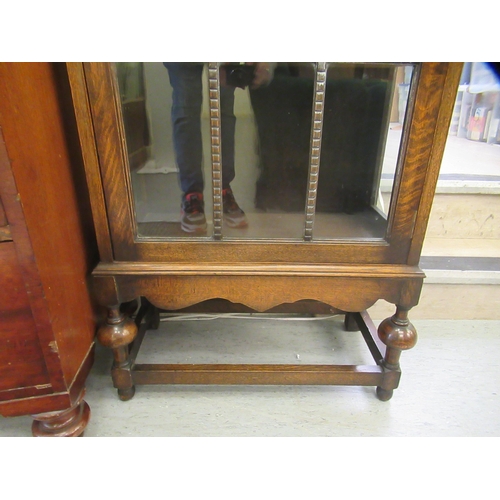 221 - A 1930s oak display cabinet with a single astragal glazed door, raised on bulbous turned legs and bl... 