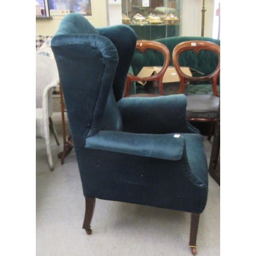 225 - An Edwardian wingback chair, upholstered in blue fabric, raised on square, tapered legs and casters&... 