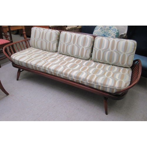 239 - An Ercol dark elm day bed with a surfboard back and fitted cushions, raised on turned legs