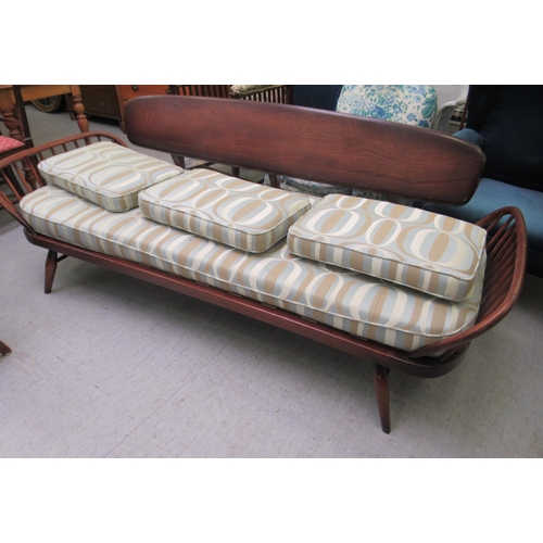 239 - An Ercol dark elm day bed with a surfboard back and fitted cushions, raised on turned legs