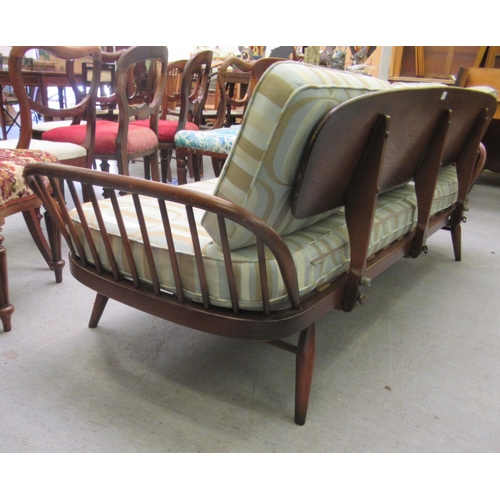 239 - An Ercol dark elm day bed with a surfboard back and fitted cushions, raised on turned legs