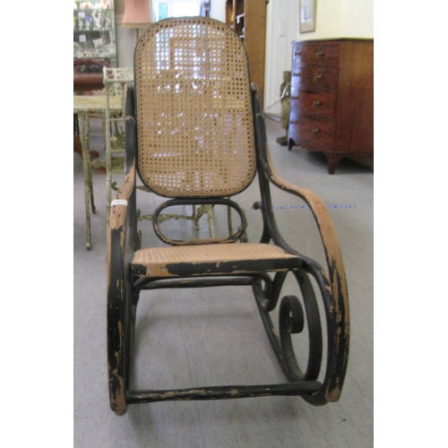 304 - An early 20thC black painted bentwood framed rocking chair with a caned back and seat