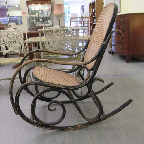 304 - An early 20thC black painted bentwood framed rocking chair with a caned back and seat