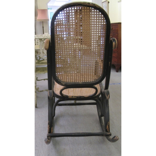 304 - An early 20thC black painted bentwood framed rocking chair with a caned back and seat