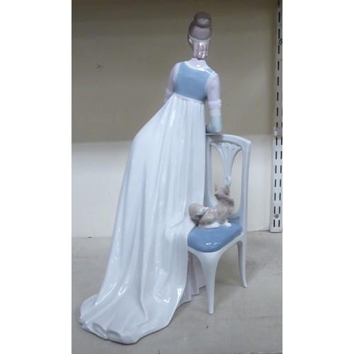 307 - A Lladro porcelain figure, a lady wearing a long gown, standing bedside a chair  model no.1276  19